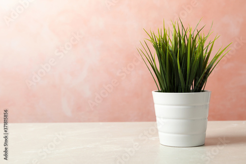 Beautiful artificial plant in flower pot on light table against color background. Space for text