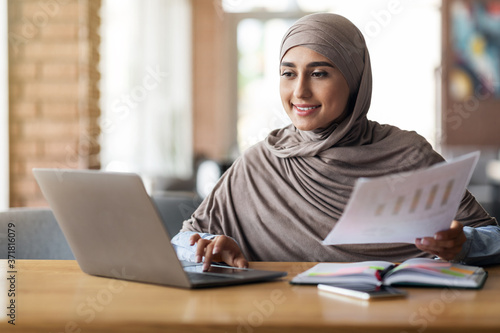 Muslim woman business analyst working on laptop at cafe
