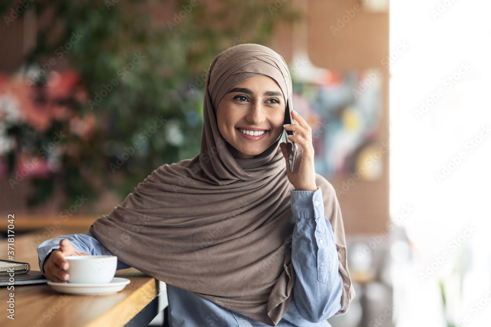 Happy muslim girl talking on phone while resting at cafe Happy muslim girl talking on phone while resting at cafe