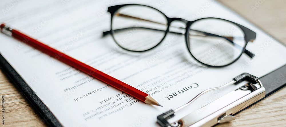 A contract on a wooden work table with glasses and a red pencil. The documents are ready for signing. Business concept. Collaboration agreement. A contract on a wooden work table with glasses and a red pencil. The documents are ready for signing. Business concept. Collaboration agreement.