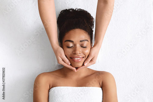 Therapist making lifting facial massage for beautiful black lady photo