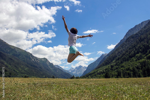 The young girl full of joy jumps against the background of mountains and a blue sky with white clouds. Expression of love for travel and nature.