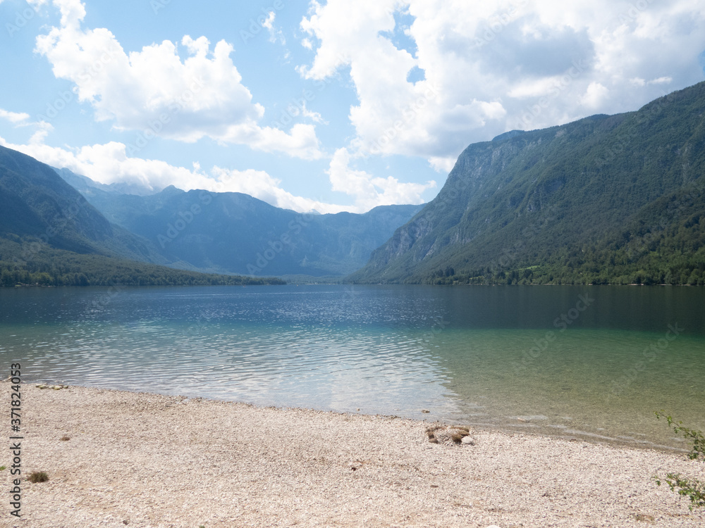 Deep-blue lake with mountains and blue sky with clouds in background and beach in the front Deep-blue lake with mountains and blue sky with clouds in background and beach in the front