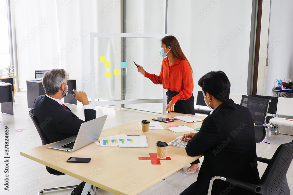 Fototapeta premium Young Asian female presenting sales graph on the board to his senior male manager and his colleagues. All wearing masks and keep distance for good health and hygiene at workplace during Covid 19