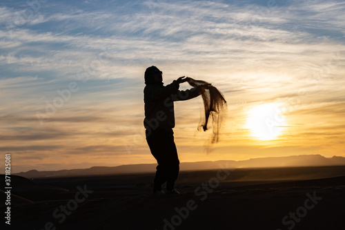 Silhouette of person jumping and throwing sand in the Sahara against a sunset