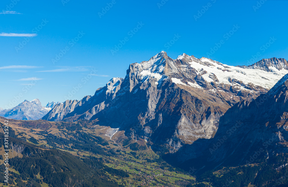 Stunning aerial panorama view of Grindelwald town with Wetterhorn peak of Swiss Alps on Bernese Oberland on sunny autumn day with clear blue sky from Mannlichen, Canton of Bern, Switzerland
