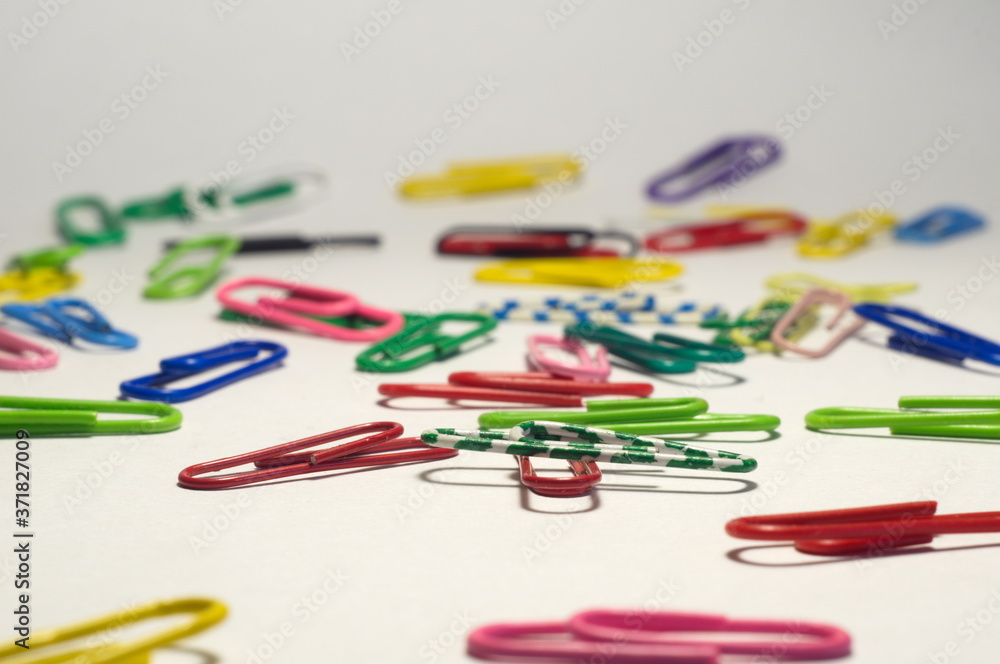 white-green paper clip on the background of other colored blurred paper clips white-green paper clip on the background of other colored blurred paper clips
