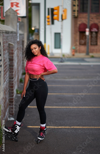 Beautiful young woman roller blades in the city wearing pink mesh shirt sitting on parking block