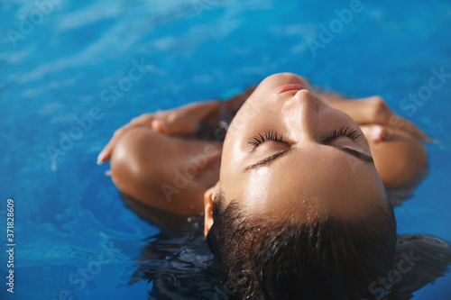 Close-up of sensual, relaxed female model sunbathing under hot sun, soaking in swimming pool. Attractive woman in bikini, close eyes and smiling pleased as enjoying cool water of poolside