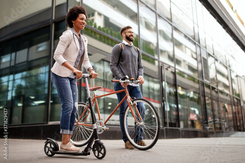 Two smiling business people driving electric scooter, bicycle going to work.