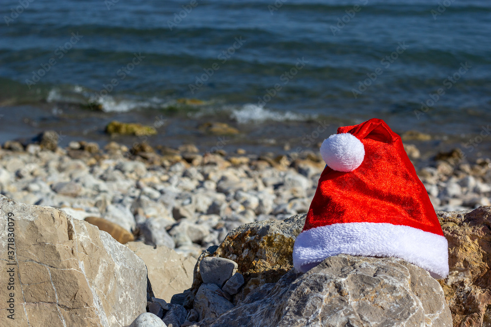 Santa's hat on a beach. Blue sky, sea and rocks. Christmas and New Year's vacation in hot countries concept. Santa's hat on a beach. Blue sky, sea and rocks. Christmas and New Year's vacation in hot countries concept.