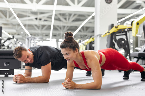 young man and woman standing in plank position at the gym, side view on fit people doing exercises together