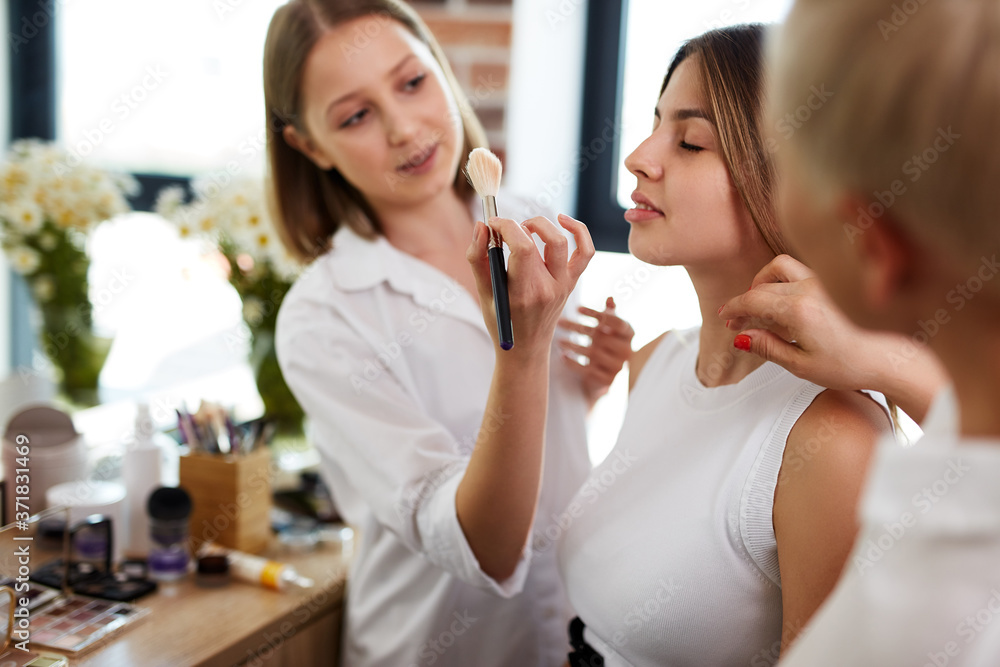 team of professional caucasian makeup artists working with young model. two make-up artist doing make-up in two hands and talk team of professional caucasian makeup artists working with young model. two make-up artist doing make-up in two hands and talk