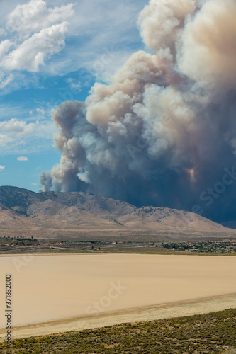 Blue and white sky puffy cumulonimbus clouds and smoke from a large wildfire in the desert muddy lake in foreground