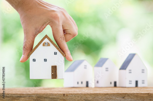 фотографія A woman shopping for a new home is hand hold at one of the houses on the table in the backyard, Saving money or loan for business Investment real estate concept