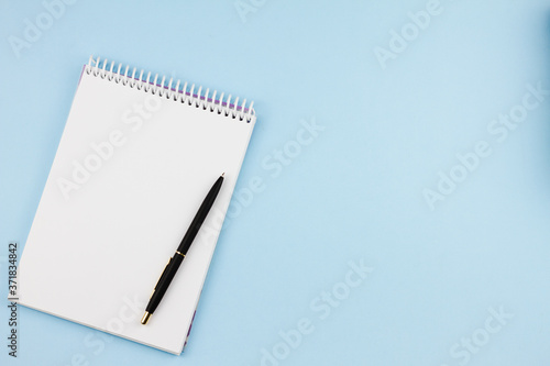 White blank notebook with a black branded pen on a light blue background. View from above. Photo concept.