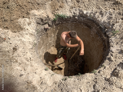 A man with a shovel in a deep hole. A worker digs a hole in the ground. The man dug a trench.