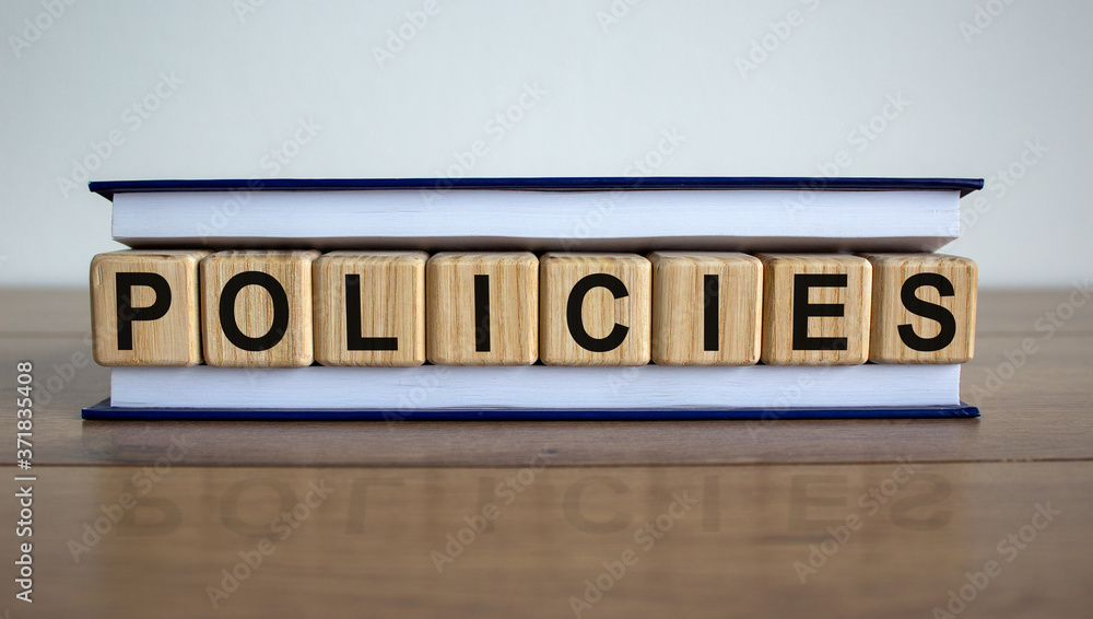 Obraz premium Concept word 'policies' on wooden cubes between pages of a book on a beautiful wooden table. White background. Business concept.