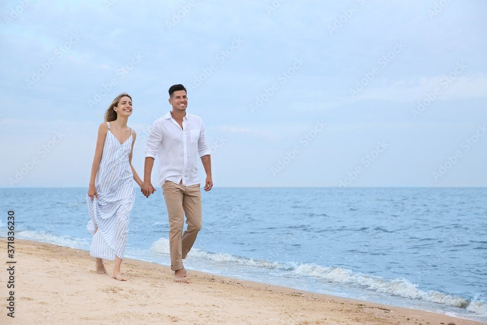 Happy couple having romantic walk on beach. Space for text