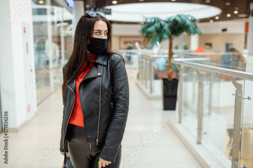 A girl with a medical black mask is walking along a shopping center. Coronavirus pandemic. A girl in a protective mask is shopping at the mall