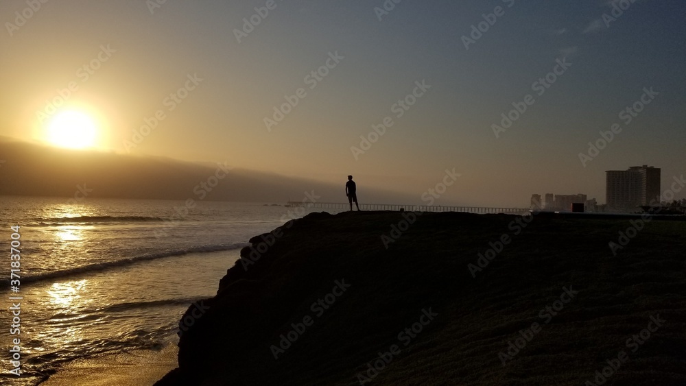 Person looking out over the ocean from a cliff at sunset