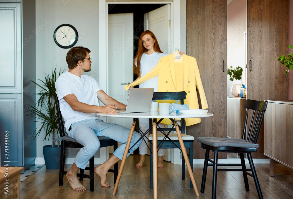 attractive lady show new clothes to working husband, young redhead woman came from shopping, share happiness with man sitting with laptop attractive lady show new clothes to working husband, young redhead woman came from shopping, share happiness with man sitting with laptop
