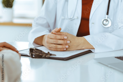Unknown woman-doctor and patient discussing something while sitting at the table in clinic, close-up. Medicine concept