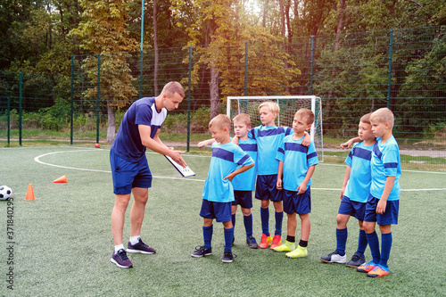 Young coach stand with clipboard and teaches little children the strategy of playing on the football field.  © Serhii