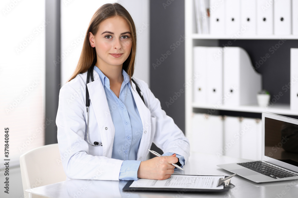 Doctor woman filling up medical form while sitting at the desk in hospital office. Physician at work. Medicine and health care concept Doctor woman filling up medical form while sitting at the desk in hospital office. Physician at work. Medicine and health care concept