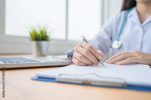 healthcare and medical care working from home concept  beautiful female Asian doctor working in home office smiling writing one clipboard diagnosing patients health using computer laptop and tablet