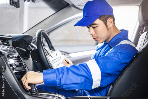 concept of male asian car mechanic holding a clipboard with checking gear box performance, checking up on the car interiors, for diagnostics and repair wearing blue overall for safety and using a pen