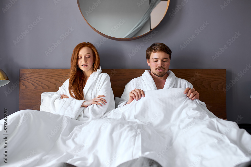 girl waiting for the first step from a man, lying on bed. caucasian redhead girl and bearded man sit keeping silence