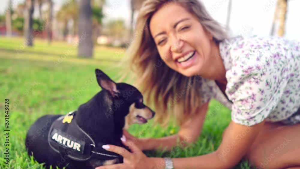 Small dog named Artur with owner, young woman, relaxing on the grass in park with palm trees. Slow motion. Dog and human love Small dog named Artur with owner, young woman, relaxing on the grass in park with palm trees. Slow motion. Dog and human love