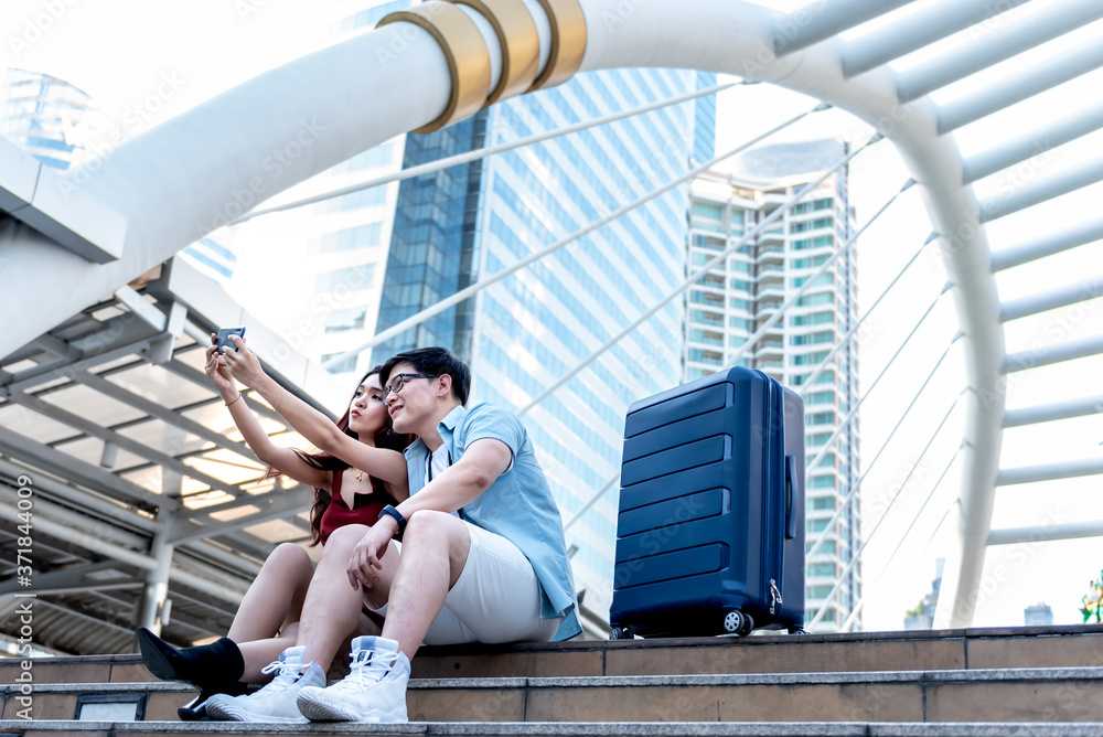 Couples, Asian tourists using mobile phones Take a selfie While they wait for the electric train on the station, with blur of Christmas tree and tall building background, concept to couples on holiday
