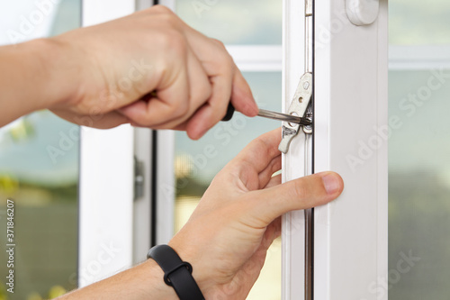 handyman adjusting white pvc plastic window indoors. worker using screwdriver to repair upvc window. homework maintenance