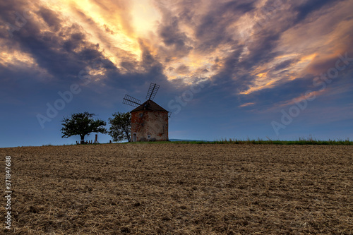 Panorama of the landscape on which is the old mill. In front of the grinder is a field and there are dramatic clouds in the sky at sunset.