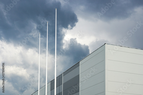 the facade of a new building and three flagpoles without flags on a background of gray storm clouds