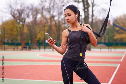 Girl athlete training using trx on sportground. Mixed race young adult woman do workout with suspension system. Healthy lifestyle. Stretching outdoors playground.