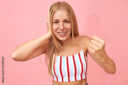 Portrait of mad annoyed young woman in striped top covering ear and making warning gesture with clenched fist, threatening noisy neighbor from upstairs because of loud music, ready to punch © Anatoliy Karlyuk
