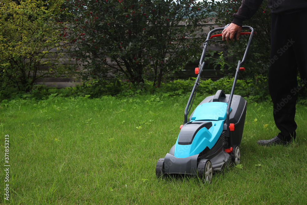 Obraz premium Lawn mowing. Man holding the handle of a lawn mower
