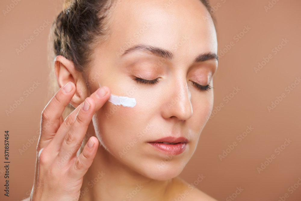 Young gorgeous female applying rejuvenating facial cream on undereye area Young gorgeous female applying rejuvenating facial cream on undereye area