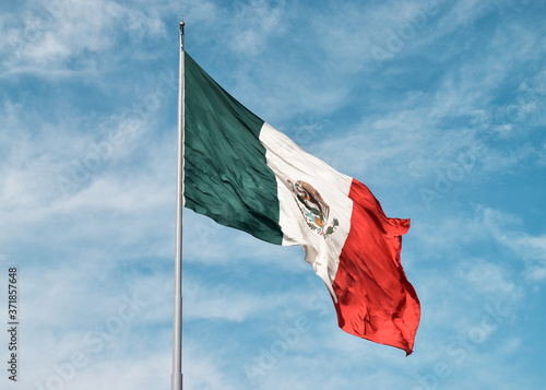 Foto Close-up of a mexican flag flying with the wind on the top of a flagpole with a blue sky and clouds as background