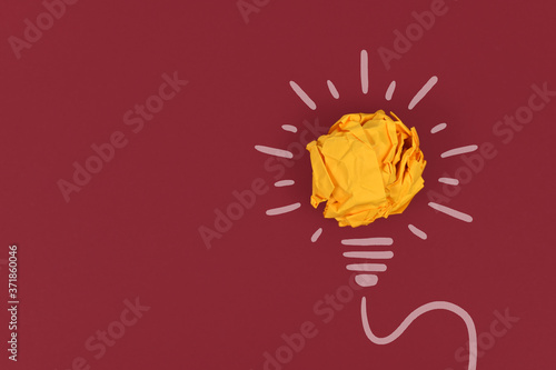 Idea concept with lightbulb made out of yellow crumbled paper ball and drawn white lines on dark red background