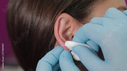 Doctor woman conducts ear piercing procedure for client.