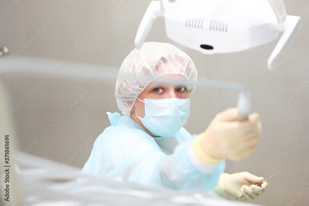 The dentist is holding a tool in his hand. Photo in the operating room. A doctor in a protective uniform and a medical mask. Copy of the space. The dentist is holding a tool in his hand. Photo in the operating room. A doctor in a protective uniform and a medical mask. Copy of the space.