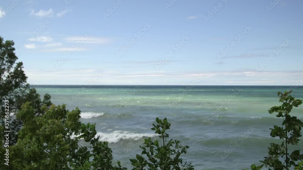 Blue green aqua water and waves through Shoreline and trees foliage, background water bright sky and clouds Lake Huron Ontario Blue green aqua water and waves through Shoreline and trees foliage, background water bright sky and clouds Lake Huron Ontario