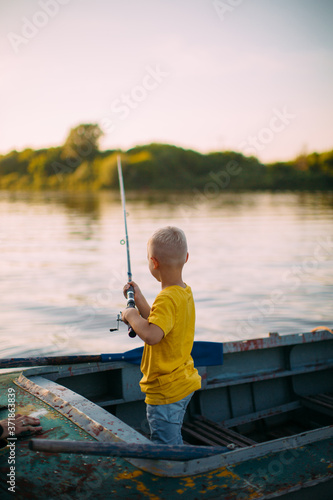 Baby boy fishing from boat on river in summertime, back view