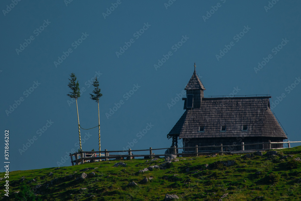 Fototapeta premium Typical old wooden chapel on the top of the hill on Velika planina, a mountain plateau in central Slovenia on a warm summer day.