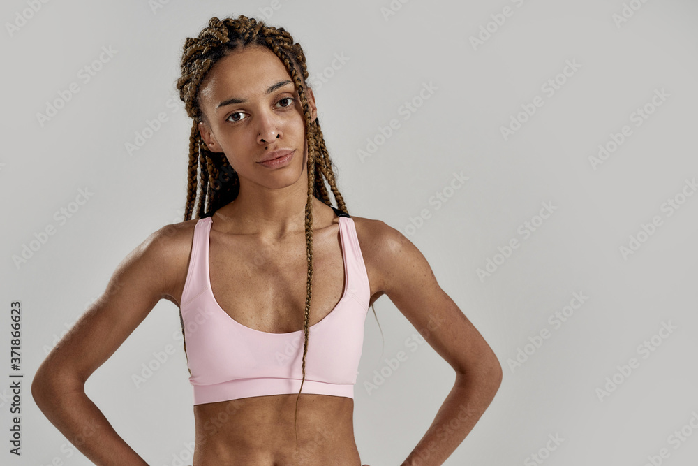 Portrait of young sportive mixed race woman in sportswear looking at camera while posing isolated over grey background. Healthy lifestyle and sports concept Portrait of young sportive mixed race woman in sportswear looking at camera while posing isolated over grey background. Healthy lifestyle and sports concept