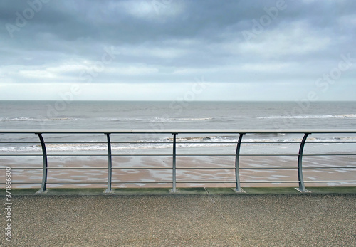 metal railings on the seafront in blackpool with waves breaking on the beach under a cloudy sky © Philip J Openshaw 